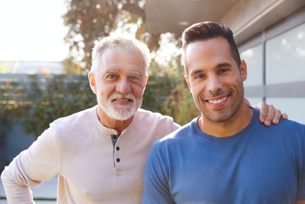 Portrait Of Loving Senior Hispanic Father With Adult Son In Garden At Home