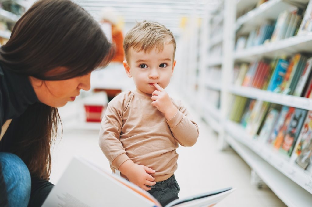 Cute baby boy toddler child in bookstore with mother with open book
