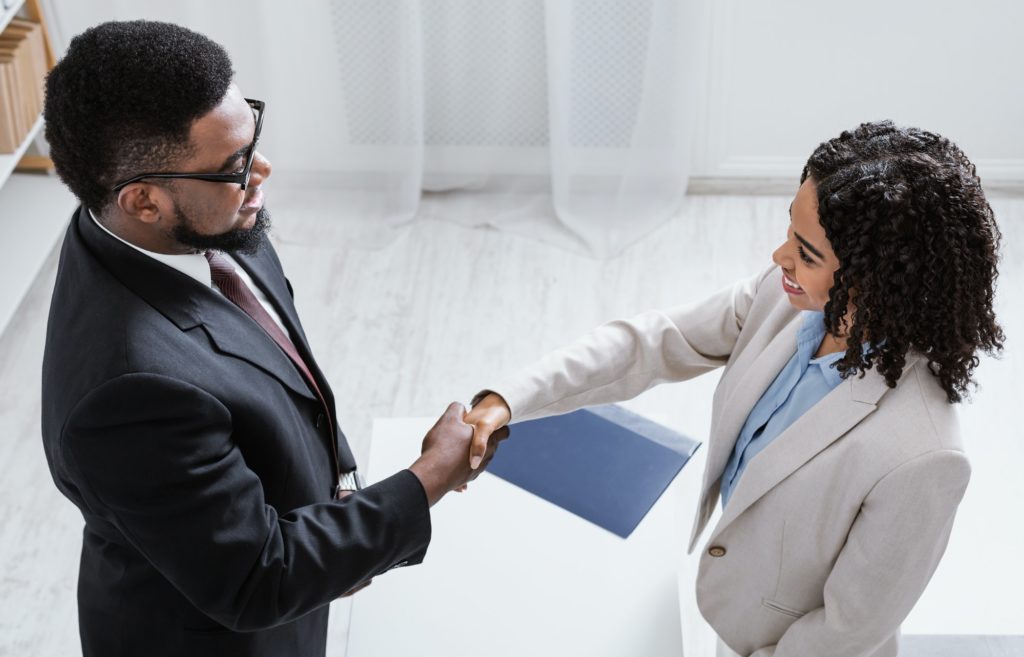Human resources manager shaking hands with successful vacancy applicant at office, above view