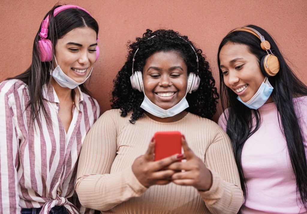 Young latin women with headphones wearing safety mask under chin for coronavirus